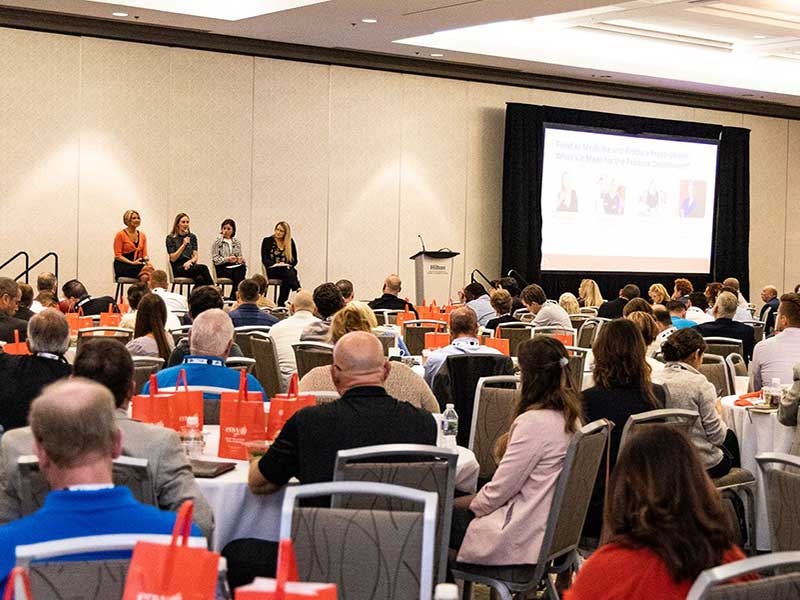 Attendees of the 2023 IFPA Retail Conference listen as four panelist present their presentation in a large banquet room.