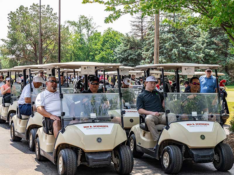 A large number of golf carts full with golfers lined up and read to proceed.